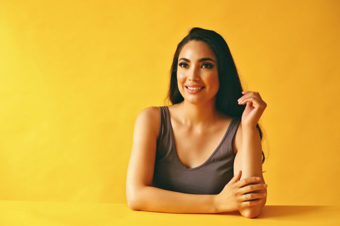 Smiling Hispanic woman looking away from camera with her hand up and sitting in yellow room