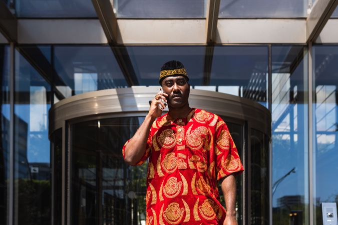 Black male in traditional clothes talking on cellphone in street