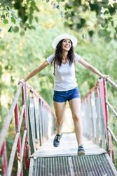 Carefree brunette female swinging herself on wooden bridge in forest