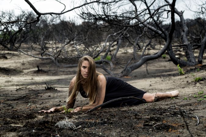 Woman posing on ground near dry trees