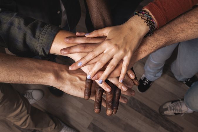 Diverse group of young people stacking hands together in a circle as a symbol of teamwork