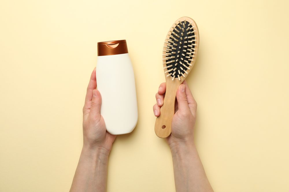 Female hands hold shampoo bottle and hair brush on beige background