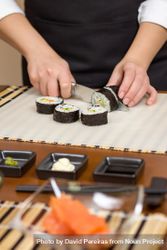 Female chef cutting Japanese sushi rolls with rice, avocado and shrimps in nori, vertical 4ZXpr0