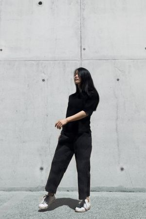 Woman in dark shirt and pants standing by the wall
