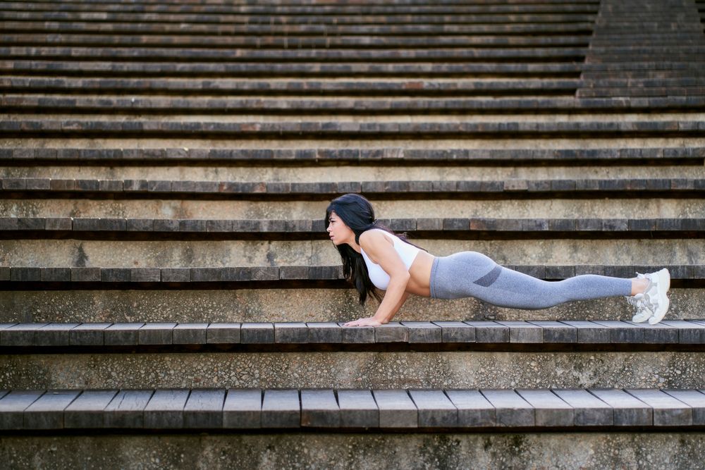 a young female fitness athlete doing push-ups on a wooden steps