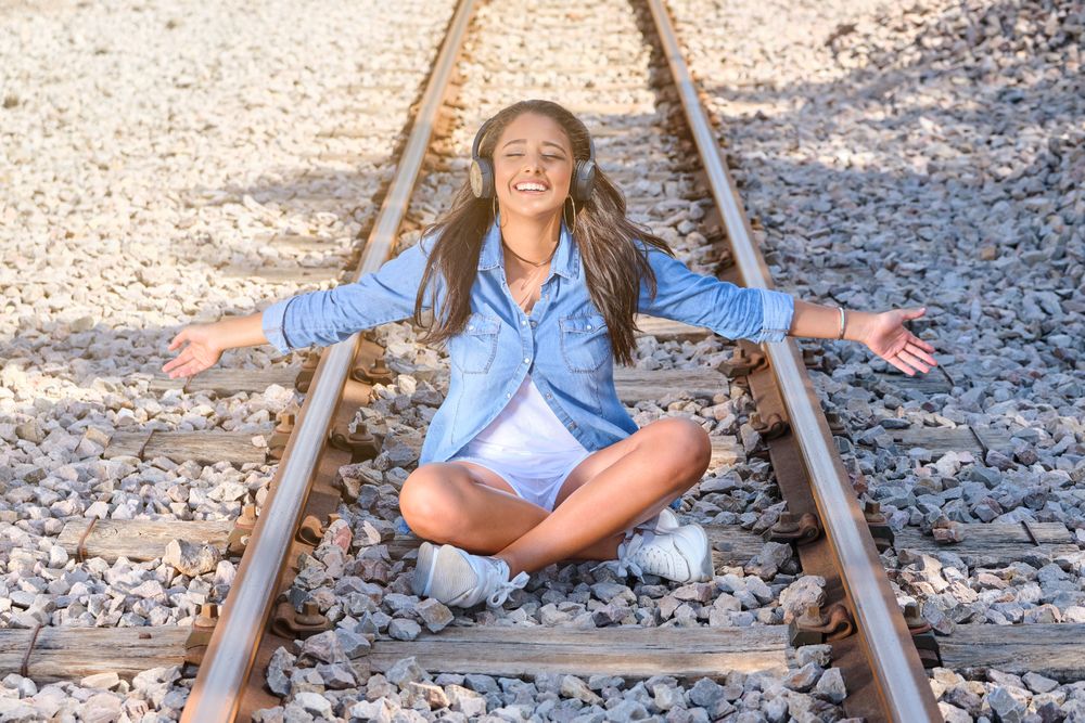 Smiling woman listening to music sitting on railroad