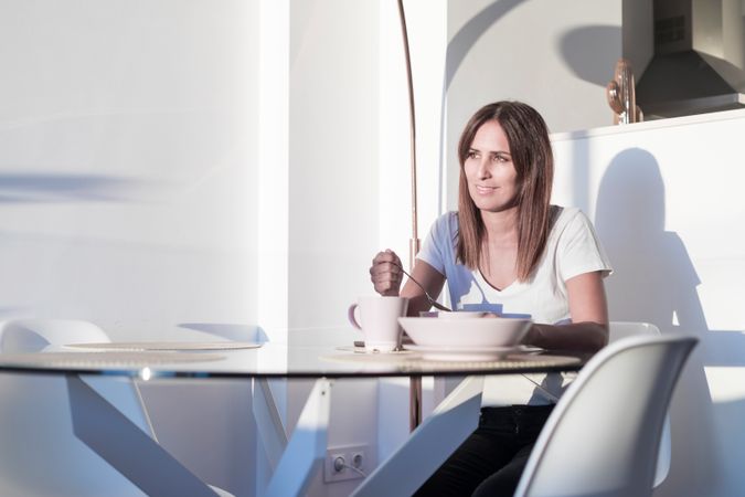 Smiling woman sitting at sunny table having bowl of cereal