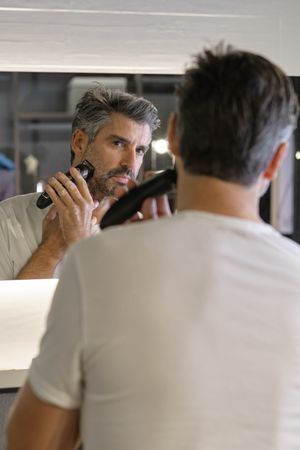 Adult male trimming beard in bathroom at home