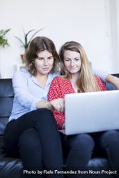 Female couple using computer while sitting on couch bYqN1G