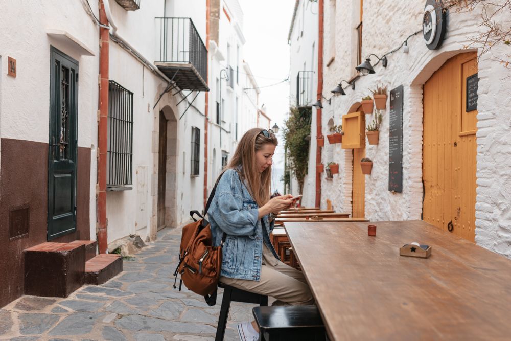Young woman in small village sitting at outside wood table looking at cell phone