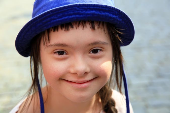 Close up portrait of beautiful little girl with blue hat smiling and looking at camera
