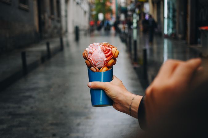 Tattooed hand holding waffle and ice cream dessert on rainy street
