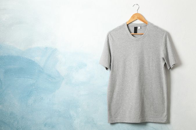 Hanger with blank gray t-shirt on blue background, space for text
