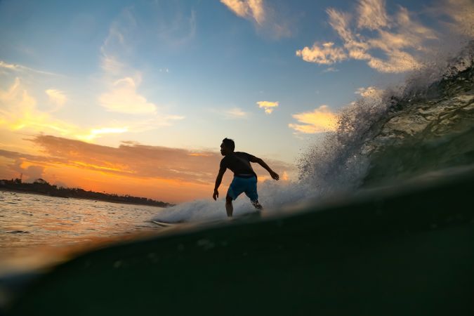 Man on surf board on waving water at sunset