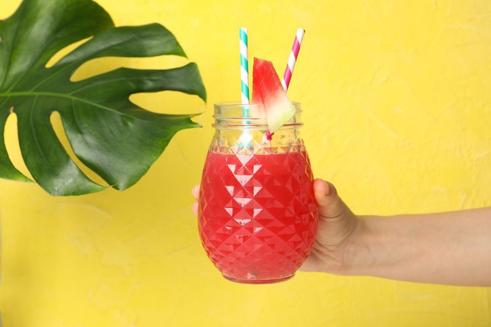 Female hand holds glass of watermelon juice on yellow background