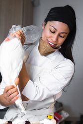 Female cook decorating cupcakes with whipped cream