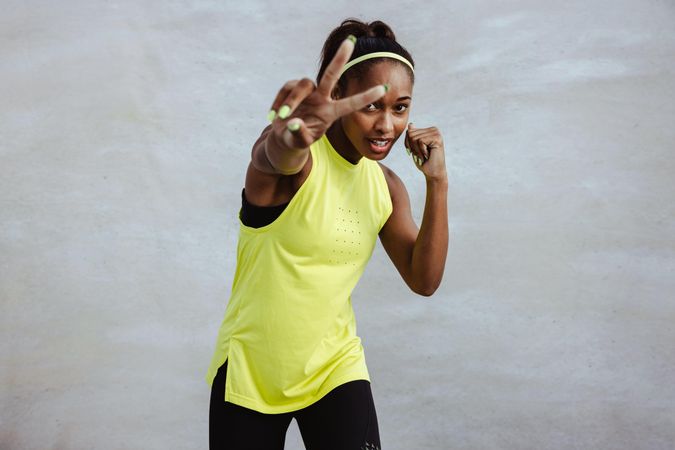 Sporty woman stretching arm out with peace sign gesture