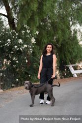 Full length shot of woman standing with her dog in front of green trees 5r9dp0