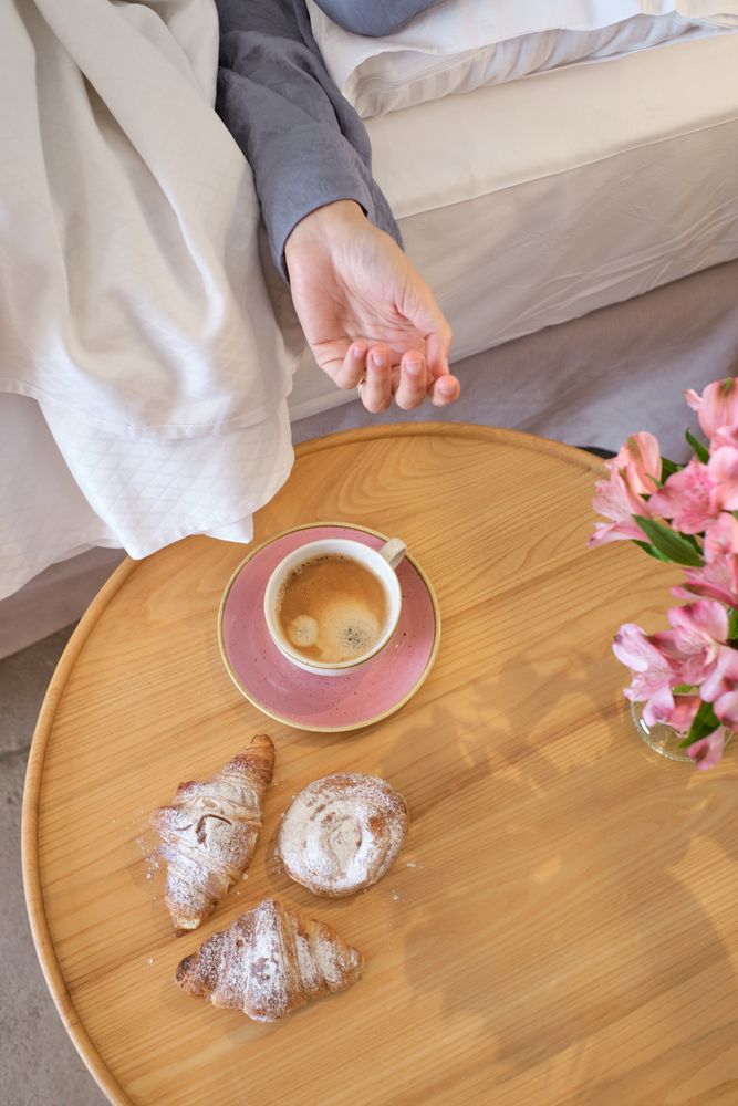 Crop female reaching out coffee cup in bedroom