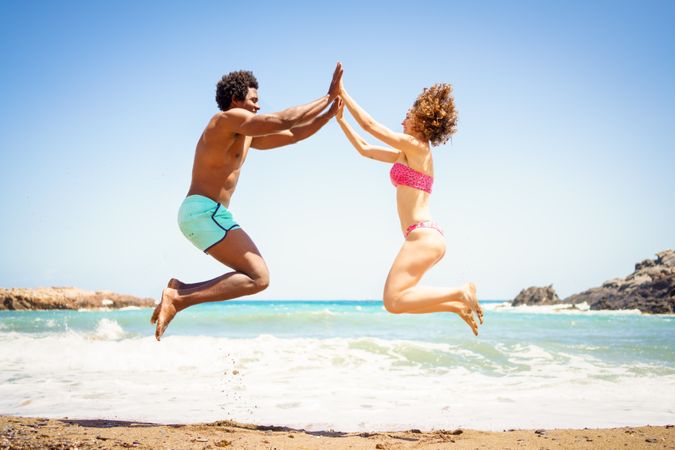 Happy man and woman jumping up and high giving at beach