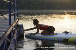 Woman launching from pier on paddleboard in the sunrise 43RYR5