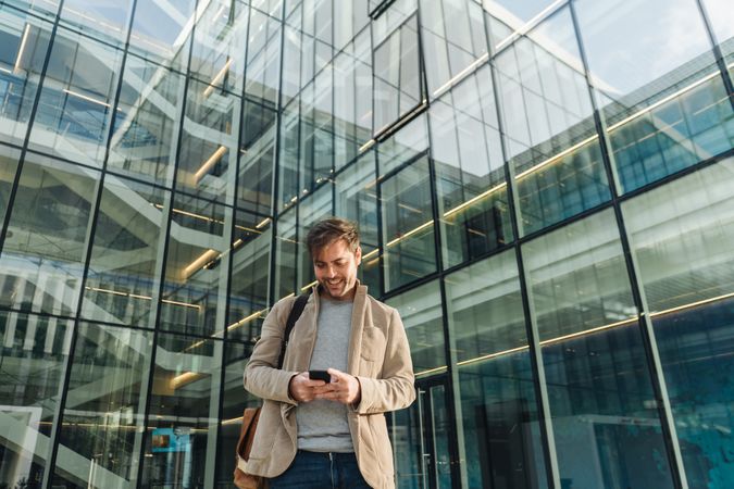 Smiling entrepreneur using smartphone outside office building