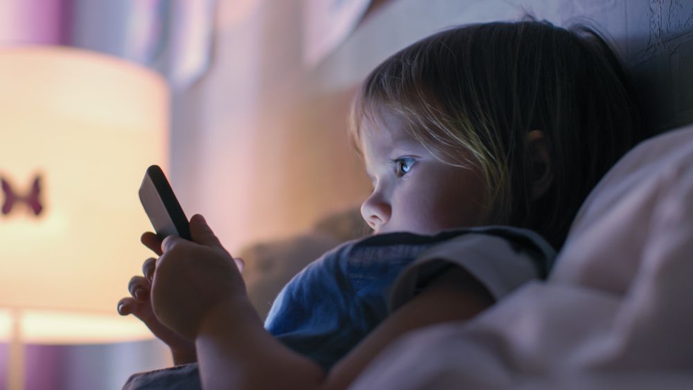 Close-up Shot of a Little Girl Watches Cartoons on a Smartphone in a Bed.