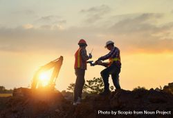 Two men wearing protective helmets standing on construction site during sunset 4NJvm4