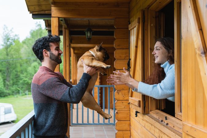 Cheerful couple playing with dog on terrace of house