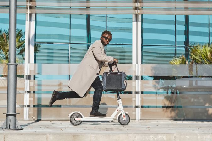 Stylish Black man with handbag riding scooter