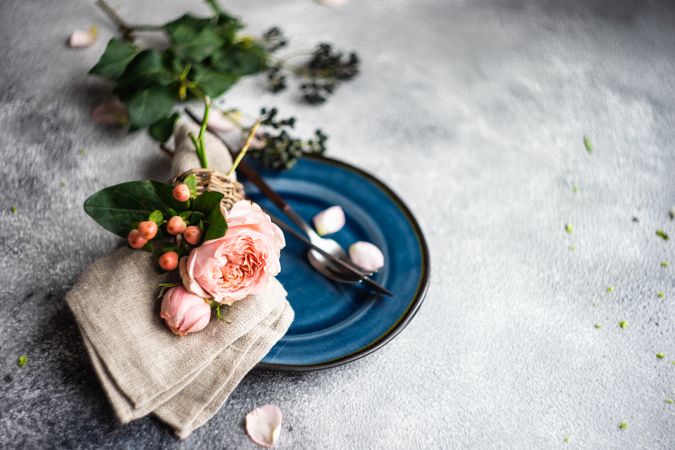 Delicate pink flowers on grey napkin and blue plate with cutlery and space for text