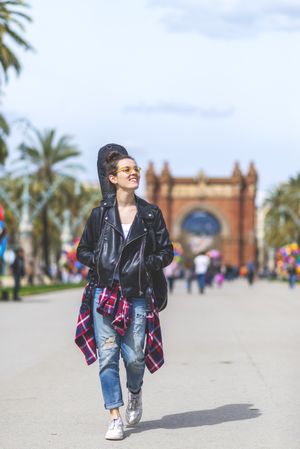 Front view of a young laughing hipster woman walking in a park in sunny day while looking away