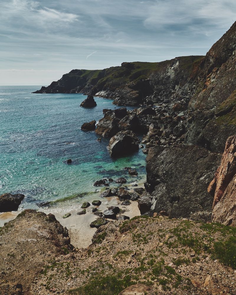 Rocky cliffs in Cornwall looking down to the sea with cloudy sky