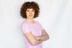 Happy female in light pink t-shirt standing with arms crossed in blank space