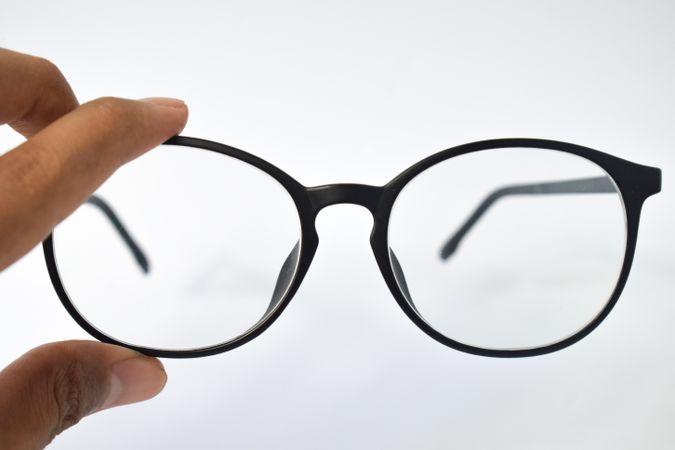 Glasses held by hand on blank background with copy space