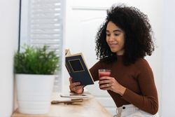 Black woman drinking smoothie and reading book in bar