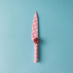 Knife wrapped in pink dotted paper with bow on blue background