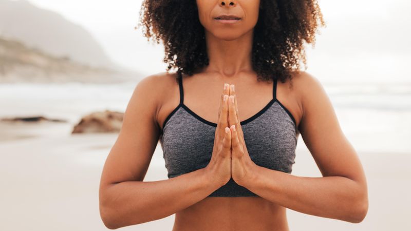 Female standing next to ocean in with hands together in prayer