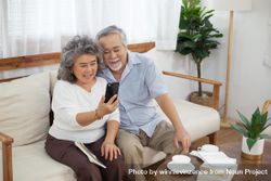 Happy Asian couple sitting on sofa using smartphone video chat bY6KD0