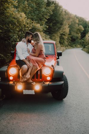Loving couple sitting on car on road near forest