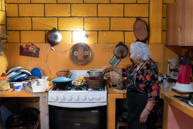 A woman is preparing red chili sauce to go with battered poblano chiles using a gas stove