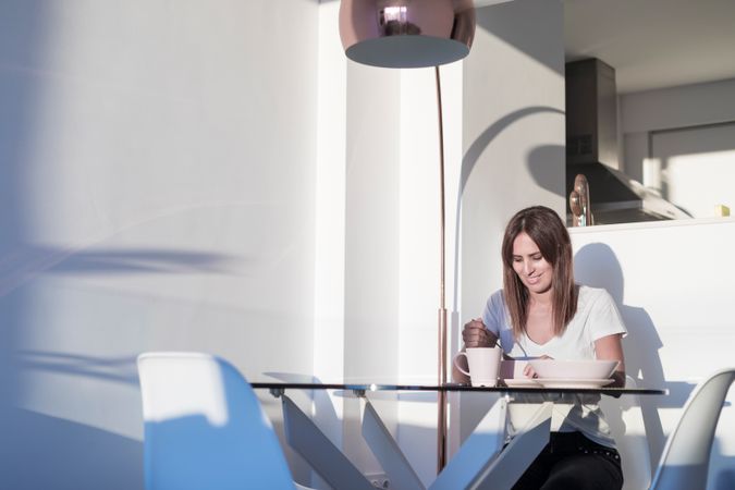 Happy woman sitting at sunny table having bowl of cereal
