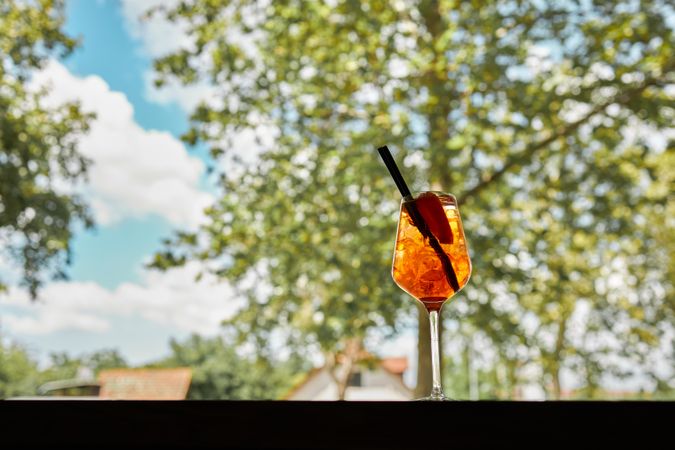 Side view of aperol spritz next to a window with tree and blue sky
