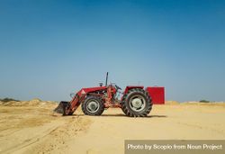 Red tractor on brown sand under blue sky 0JJyZ0