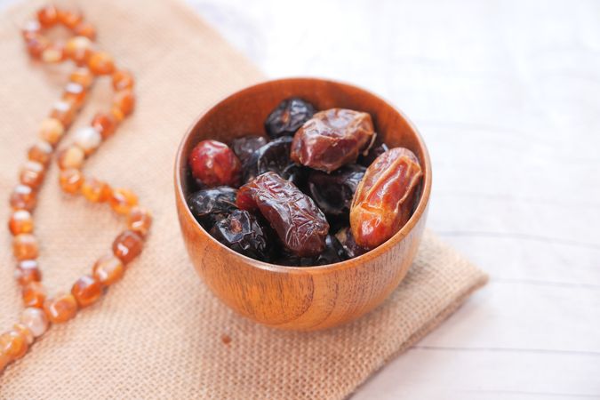 Rustic Wooden Bowl of Dates With Natural Beads on Burlap Surface