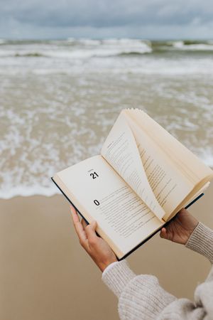 Cropped image of hand opening a book at beach