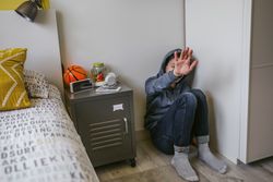 Unhappy lonely boy teenager sitting on the floor in his bedroom refusing help with his hand