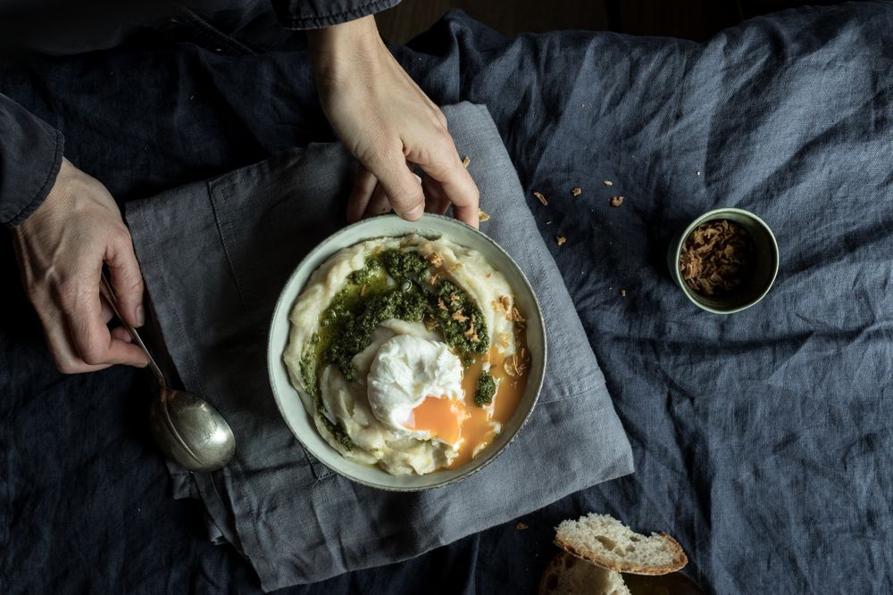 Person holding bowl with cauliflower puree with pesto and eggs