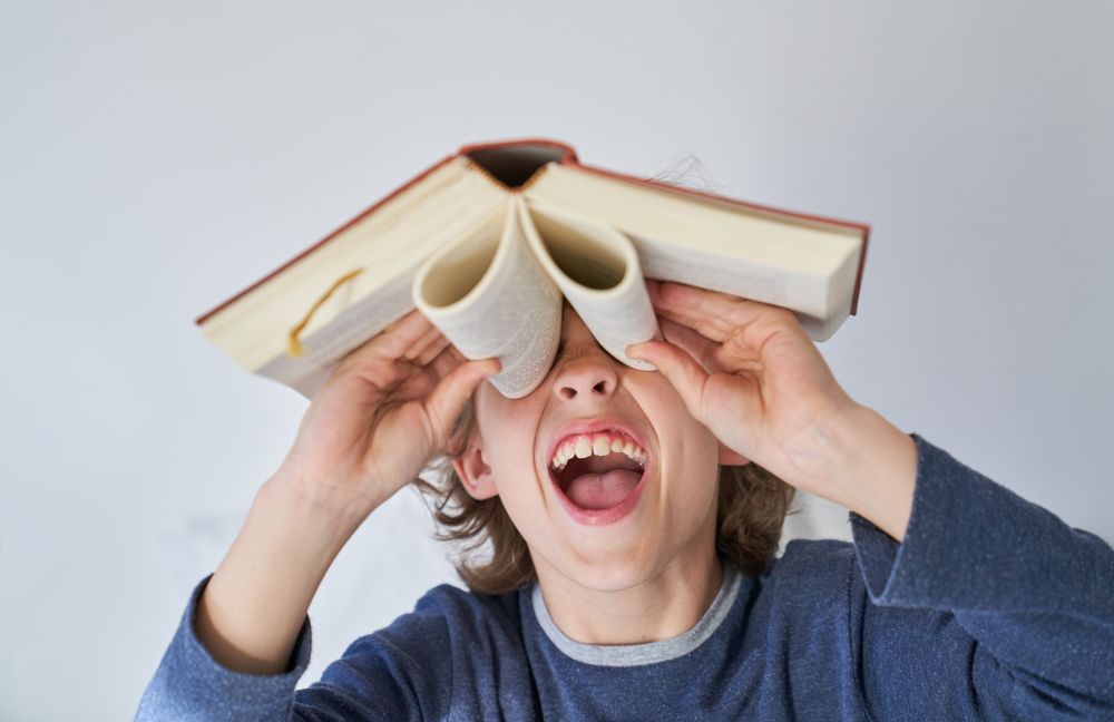 Funny boy with mouth opened looking through binoculars from book