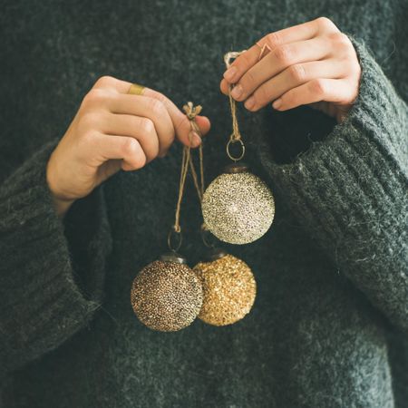 Woman holding three gold Christmas tree decoration with both hands, square crop